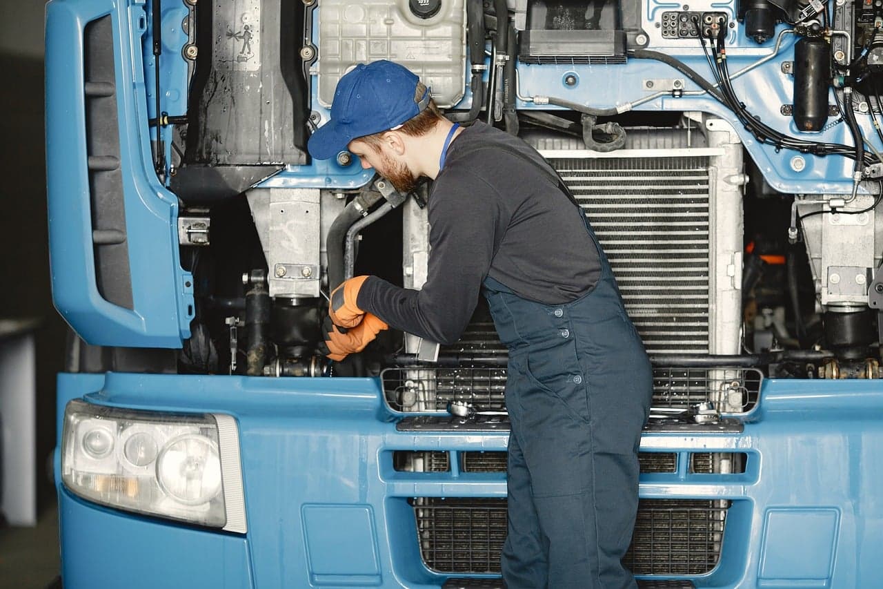 A mechanic in overalls working on the engine of a cab with the front panel open
