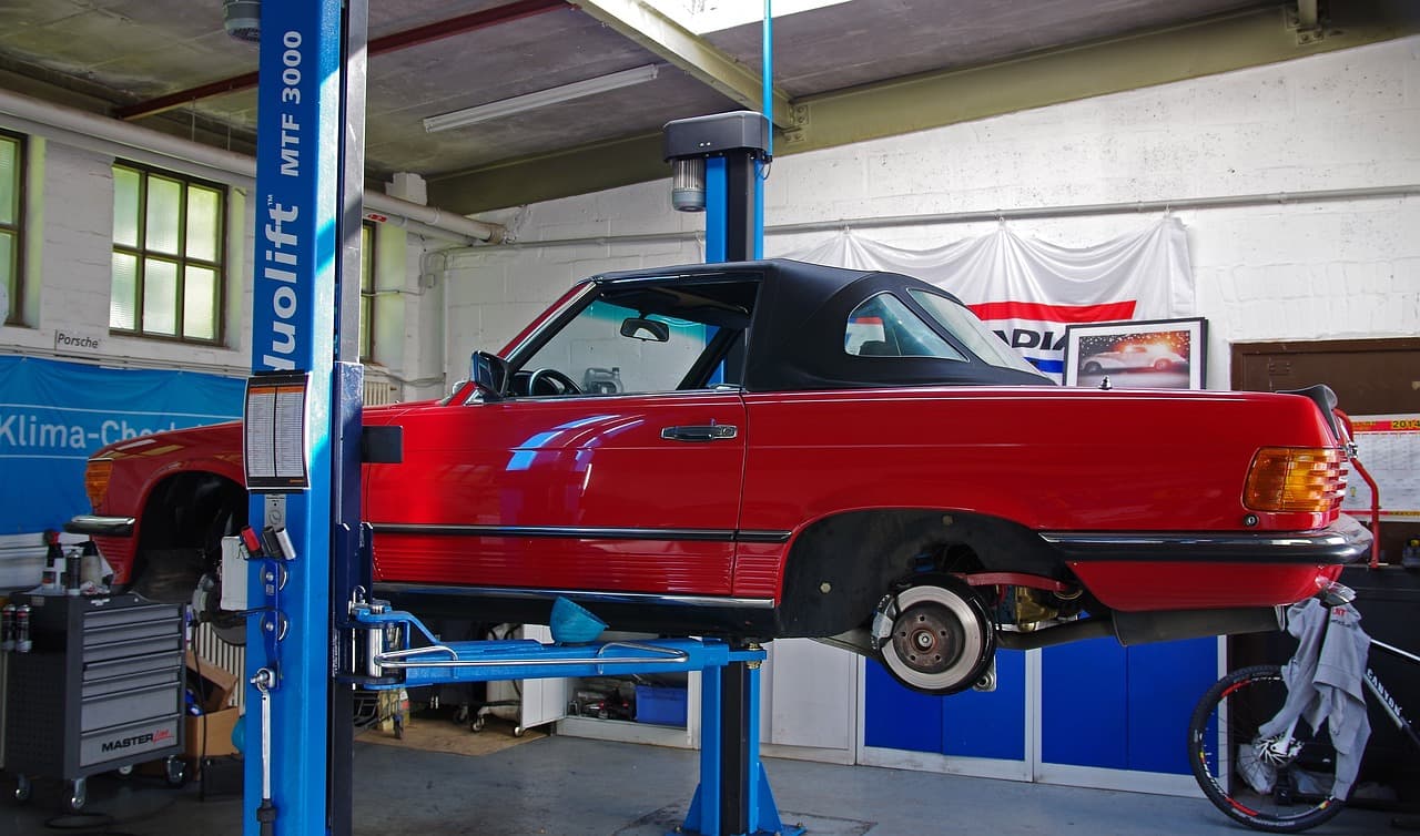 An older red convertible raised on a two-post lift with a front wheel off
