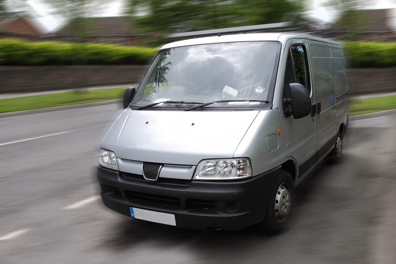 A silver panel van on the move along a hedge-lined road