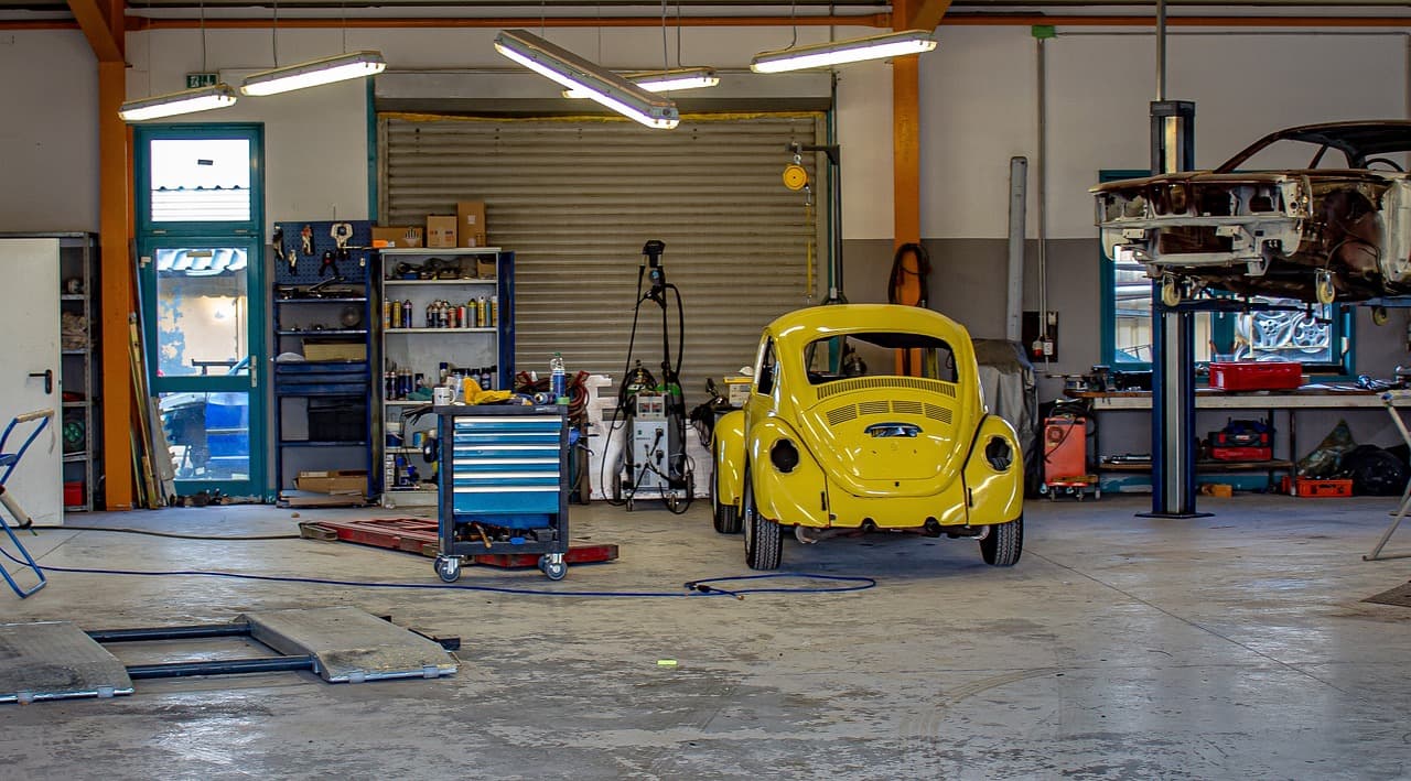 A bright, tidy workshop with a roller door, tool chests and an older car on the floor