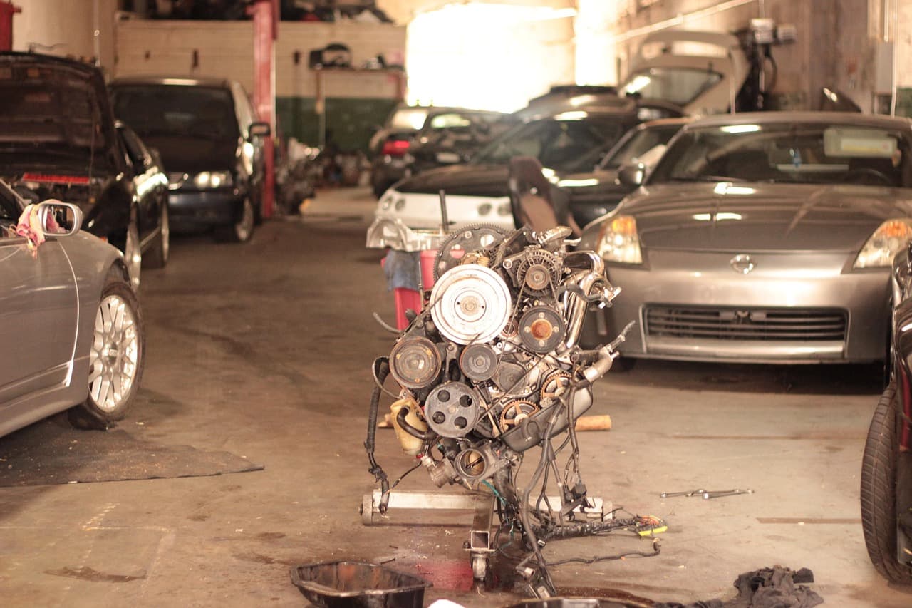 A workshop floor with an engine on a stand and cars waiting either side